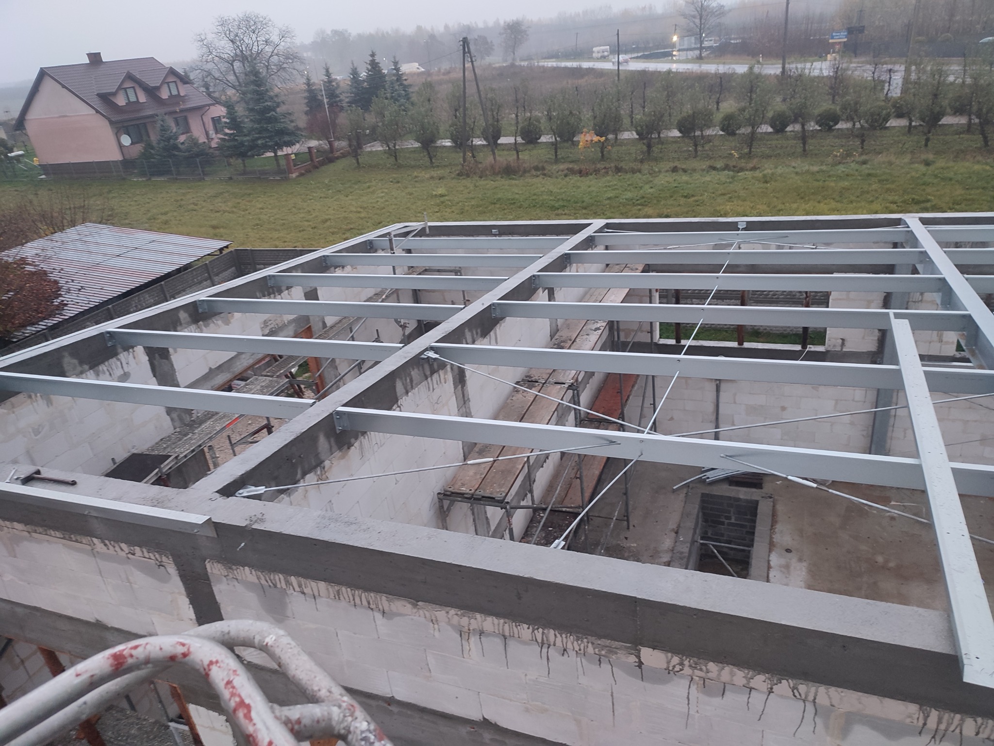 Wznoszenie konstrukcji żelbetowej: szkielet stropu z belek stalowych na murze z betonu komórkowego, widok z góry na plac budowy w pochmurny dzień.