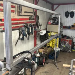 Rama z profili stalowych w trakcie spawania, zamocowana w imadle, warsztat z narzędziami w tle.