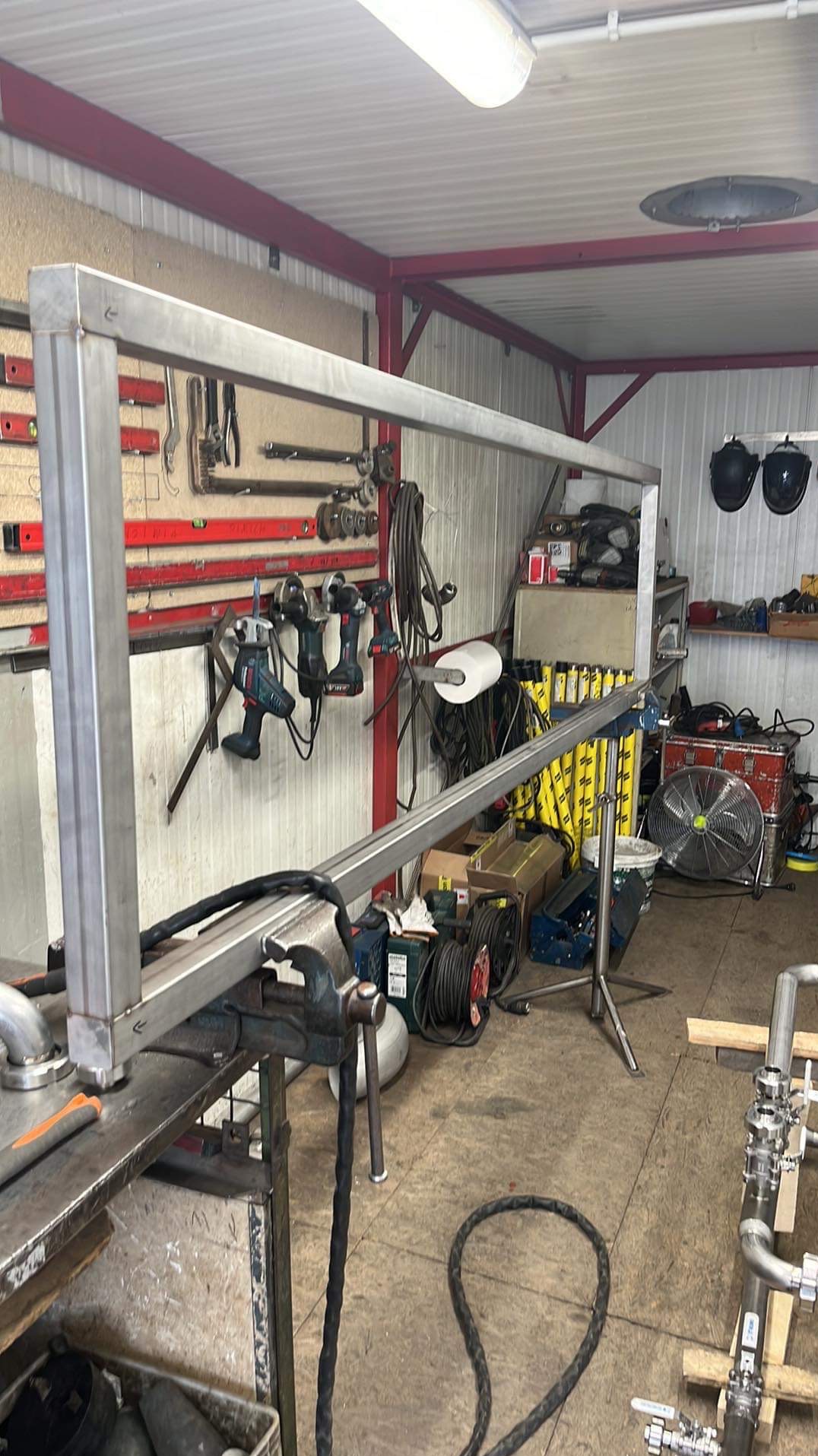 Rama z profili stalowych w trakcie spawania, zamocowana w imadle, warsztat z narzędziami w tle.