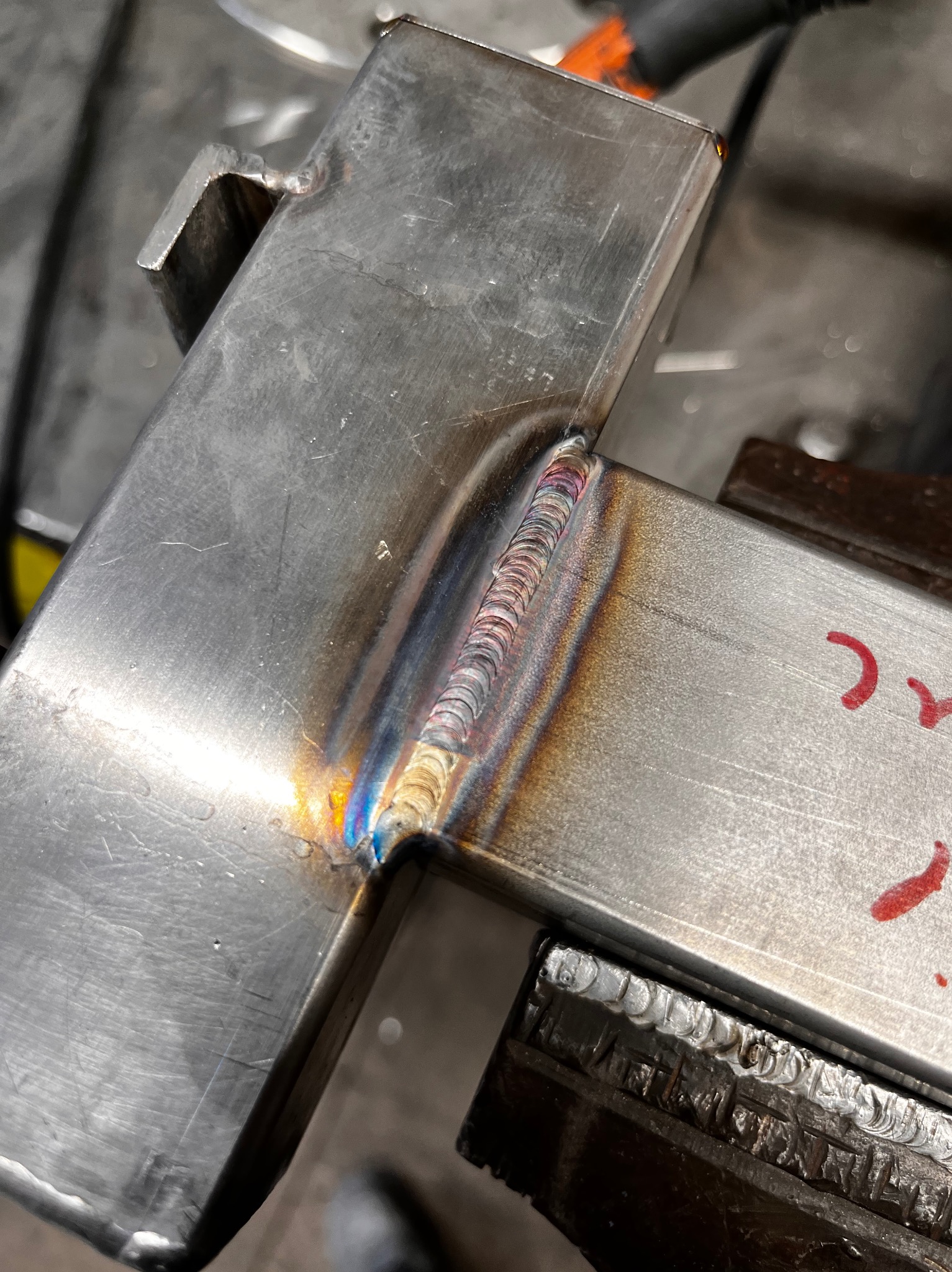 Spoina na stalowym profilu zamkniętym, widoczne tęczowe przebarwienia termiczne, całość mocowana w imadle ślusarskim.