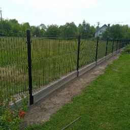 Nowoczesne ogrodzenie z paneli z podmurówką betonową, widok z zewnątrz na tle zielonego trawnika i drzew