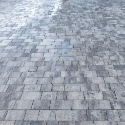 Ułożona kostka brukowa w odcieniach szarości, widoczny gumowy młotek do dobijania kostki w prawym dolnym rogu.