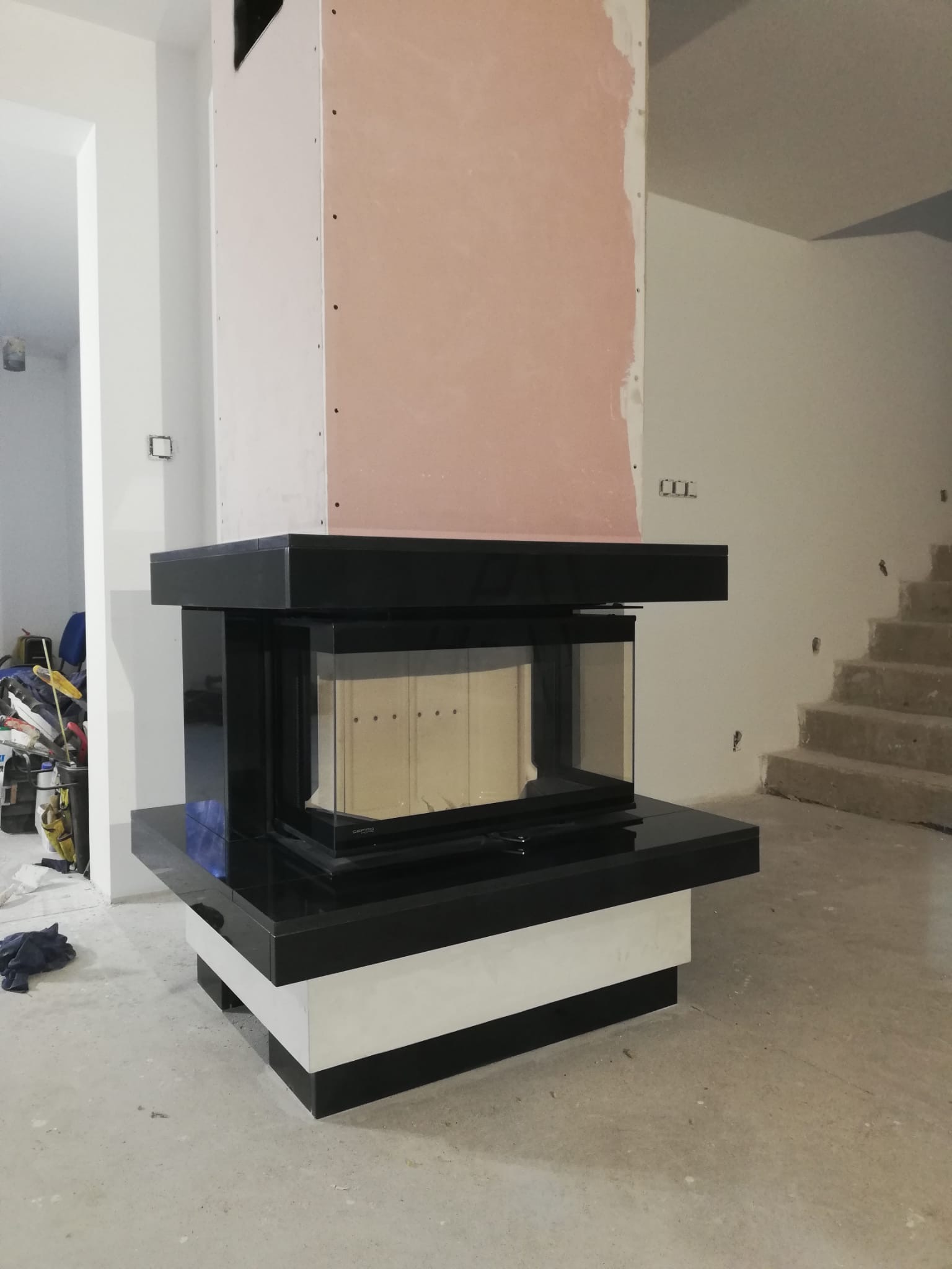 Nowoczesny, czarno-biały kominek z przeszklonym wkładem w surowym stanie, widoczny w Sulęcinie podczas montażu, ściany częściowo w stanie deweloperskim.