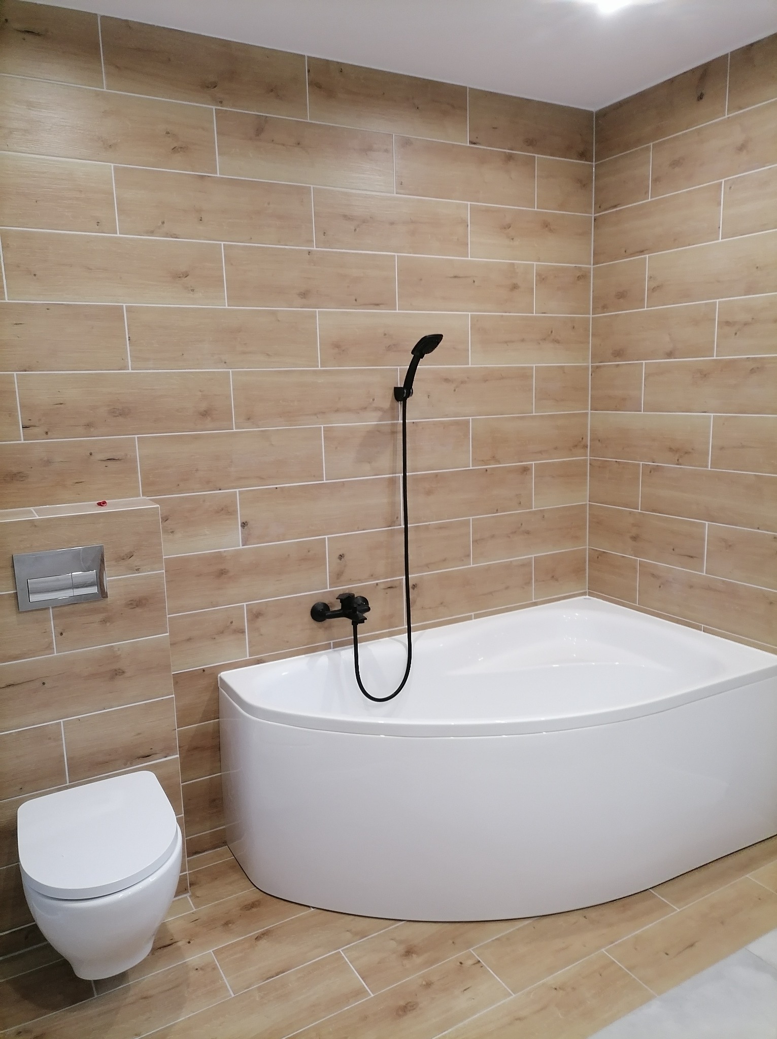 Nowoczesna łazienka w Siedliskach z wanną narożną, toaletą podwieszaną i okładziną ścienną imitującą drewno.