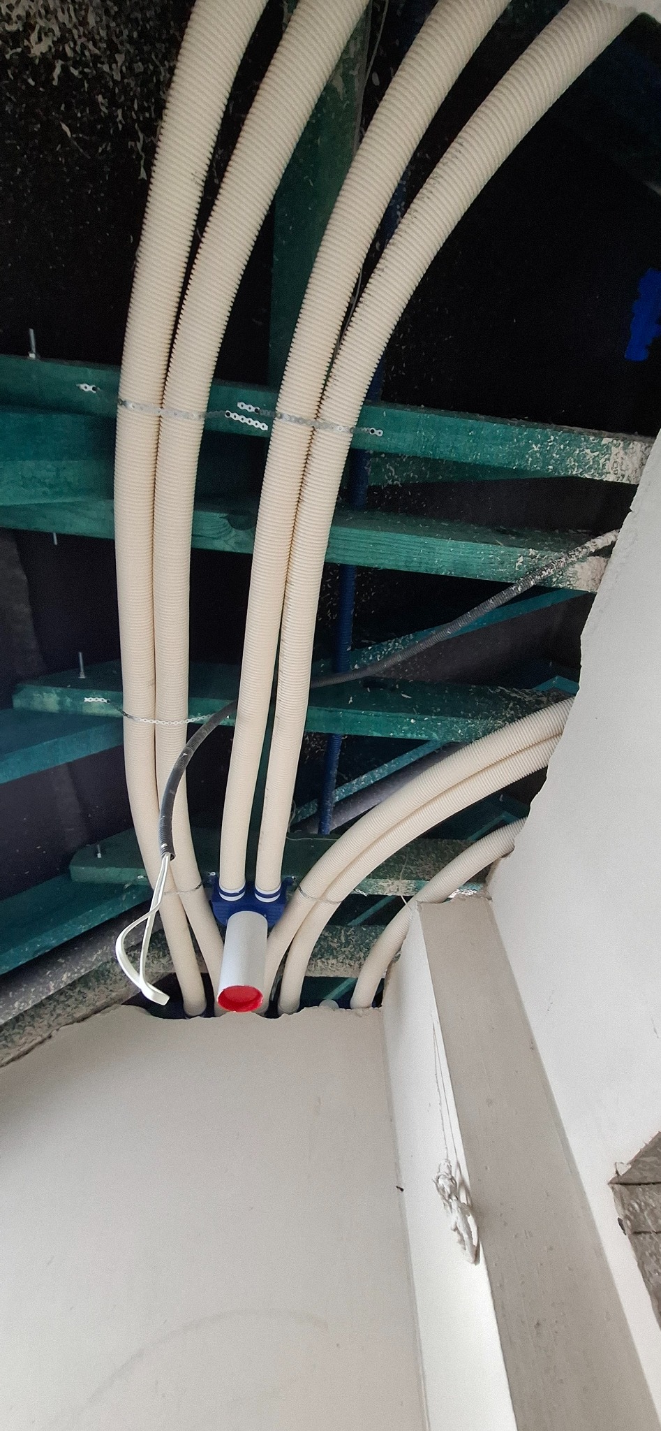 Białe, karbowane rury instalacyjne przymocowane do sufitu w Łebcz. Widoczne elementy mocujące i fragment ściany. Ujęcie z dołu, podkreślające precyzję wykonania.