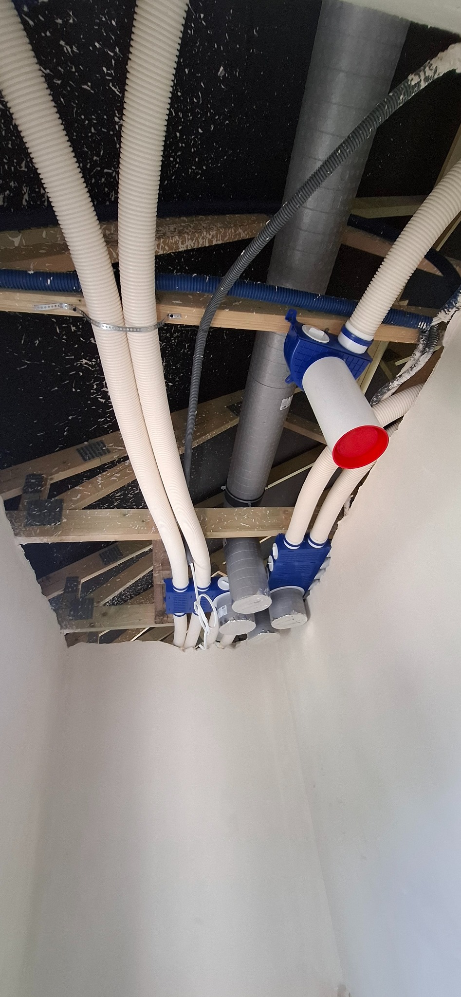 Rozprowadzenie instalacji wentylacyjnej z rurami spiro i skrzynkami rozprężnymi, widoczne elementy montażowe i izolacja. Ujęcie od dołu, w trakcie montażu.