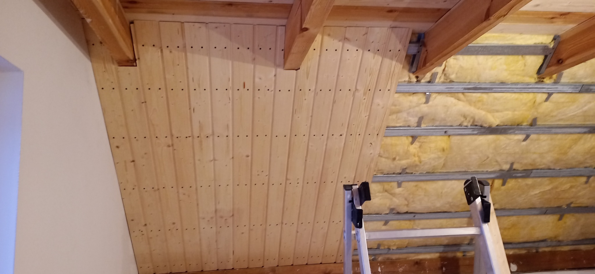 Poddasze z widoczną izolacją z wełny mineralnej i częściowo wykończone boazerią, drabina w kadrze.