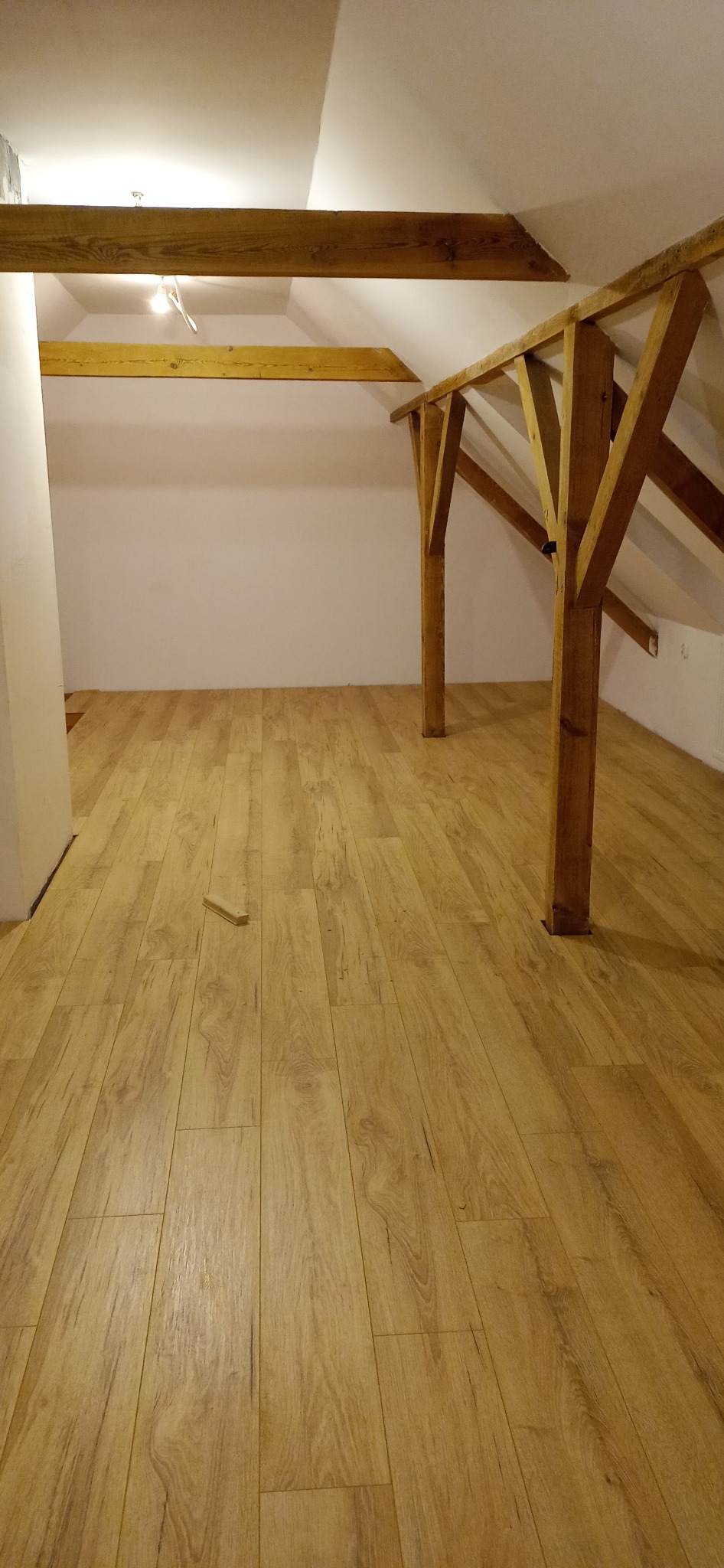 Poddasze po remoncie z drewnianą konstrukcją więźby dachowej i nową podłogą z paneli imitujących drewno, widoczny fragment listwy przypodłogowej.
