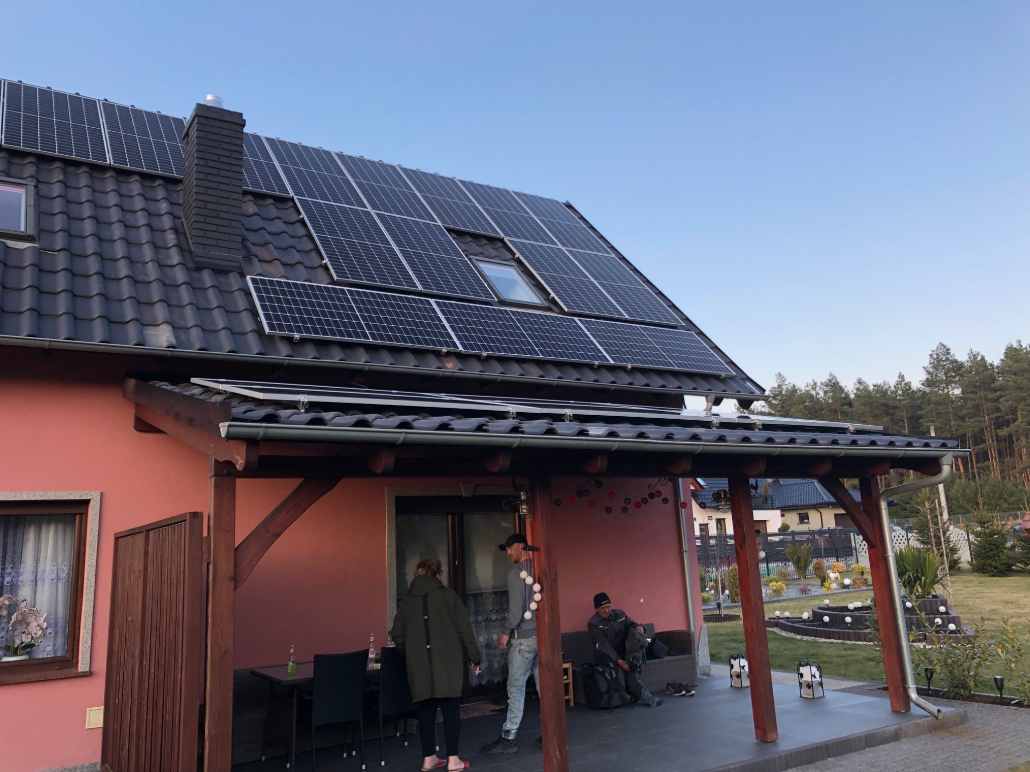 Dom w Jaworze z zainstalowanymi panelami słonecznymi na dachu; widoczni ludzie na tarasie przed domem.