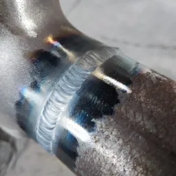 Szczegółowe ujęcie spoiny na metalowej rurze, widoczne ślady wysokiej temperatury i przebarwienia.