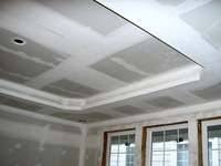 Sufit i ściany w trakcie wykończenia płytami gipsowo-kartonowymi, widoczne łączenia i szpachlowane miejsca, listwa dekoracyjna przy suficie, okna z białymi ramami.