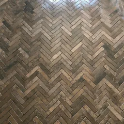 Ułożone w jodełkę, brązowe panele podłogowe z widocznym odbiciem światła w górnej części kadru.