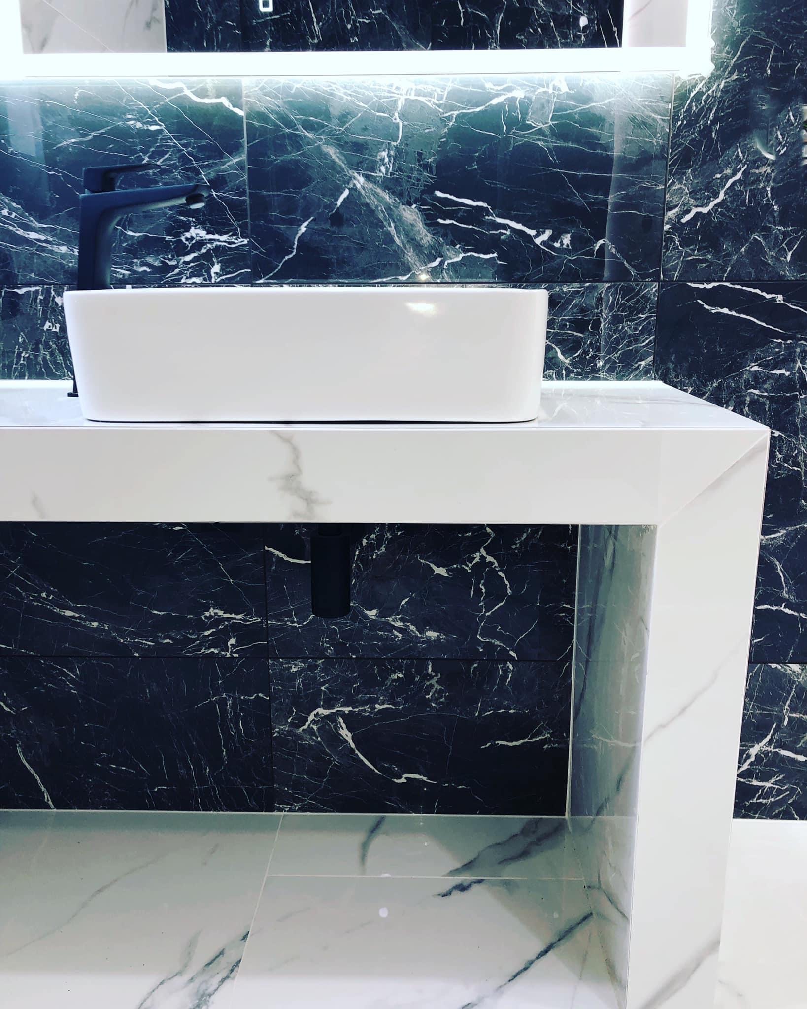 Nowoczesna łazienka z czarnymi marmurowymi płytkami na ścianie, białą umywalką nablatową i czarną baterią.