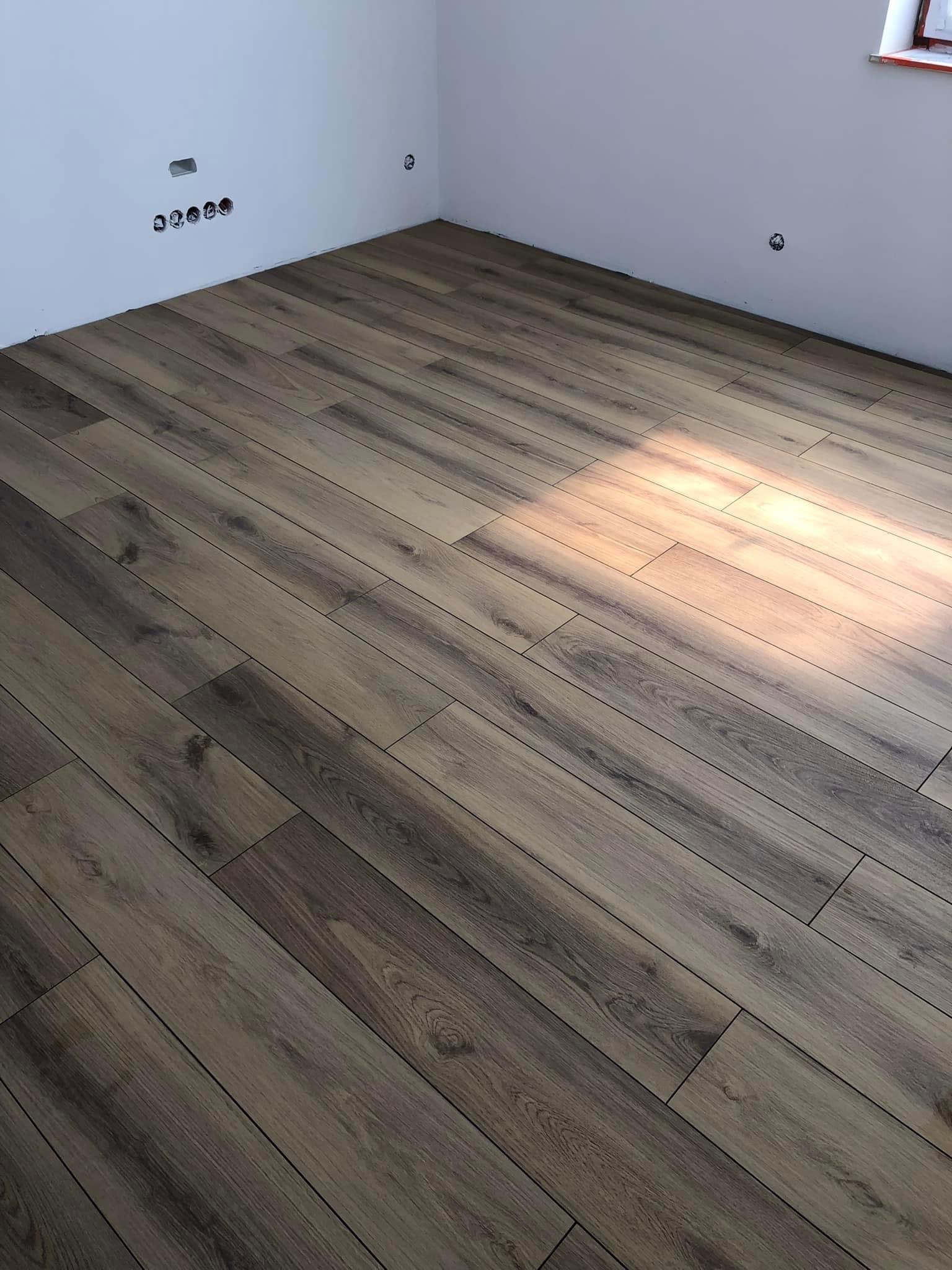 Ułożone panele podłogowe w nowym pomieszczeniu, widoczne puszki elektryczne w ścianie i fragment okna.