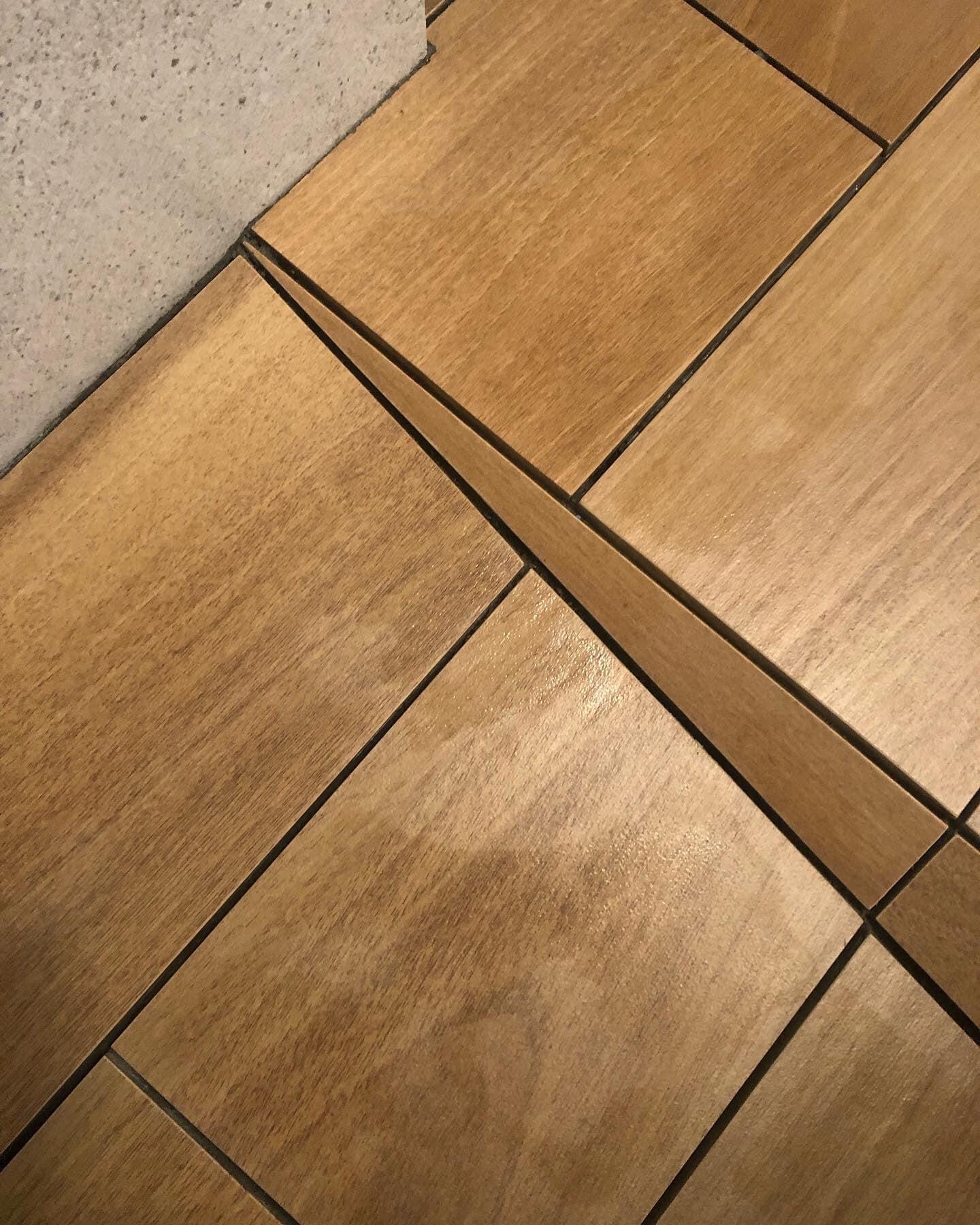 Ułożone pod kątem kwadratowe panele podłogowe z jasnego drewna, widoczna ściana w tle.