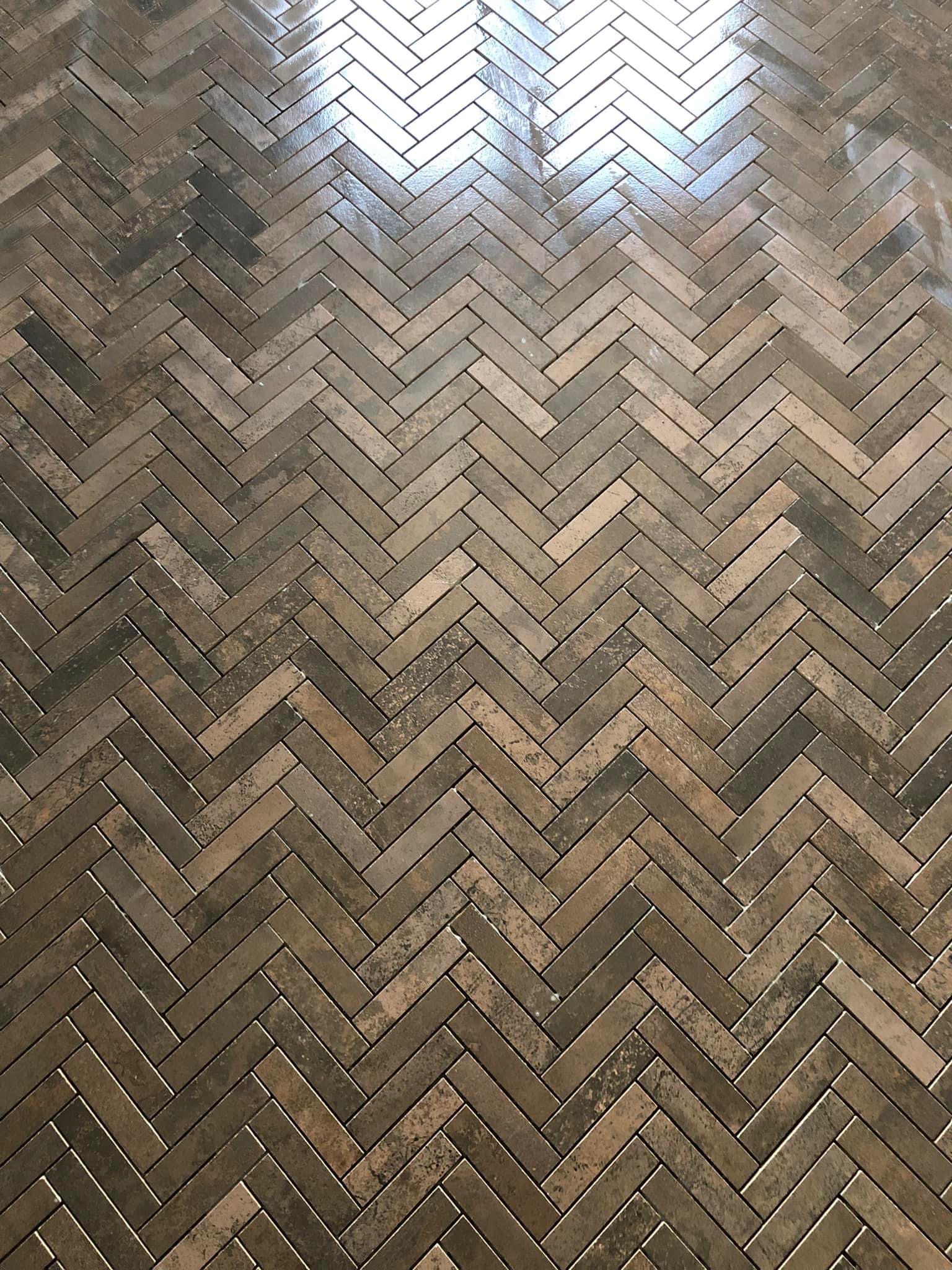 Ułożone w jodełkę, brązowe panele podłogowe z widocznym odbiciem światła w górnej części kadru.