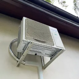 Zewnętrzna jednostka klimatyzatora marki Panasonic R32 zamontowana na wspornikach na elewacji budynku, widok z dołu, z widocznymi przewodami w izolacji.