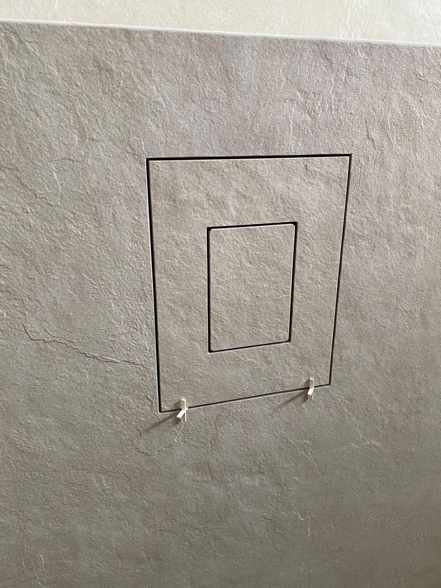 Ukryte drzwiczki rewizyjne w płytkach imitujących kamień, zamontowane z użyciem plastikowych krzyżyków dystansowych.