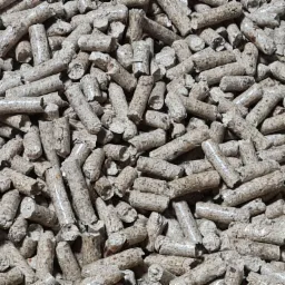 Gęsto ułożone, jasnobrązowe granulki biomasy drzewnej z widoczną strukturą włókien, tworzące teksturę na całej powierzchni zdjęcia.