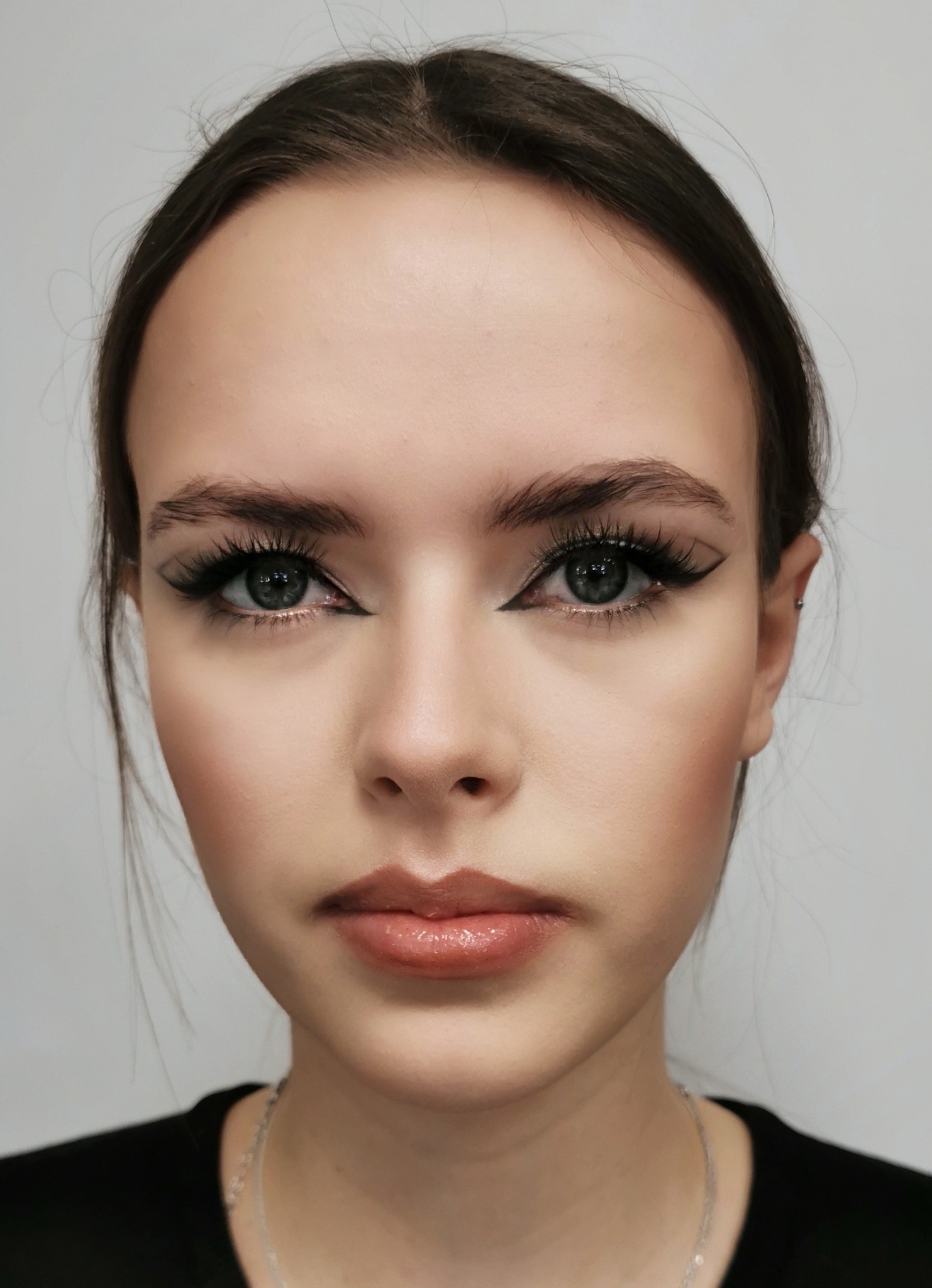 Portret młodej kobiety z precyzyjnym, graficznym makijażem oczu, podkreślonymi brwiami i błyszczącymi ustami w naturalnym odcieniu.