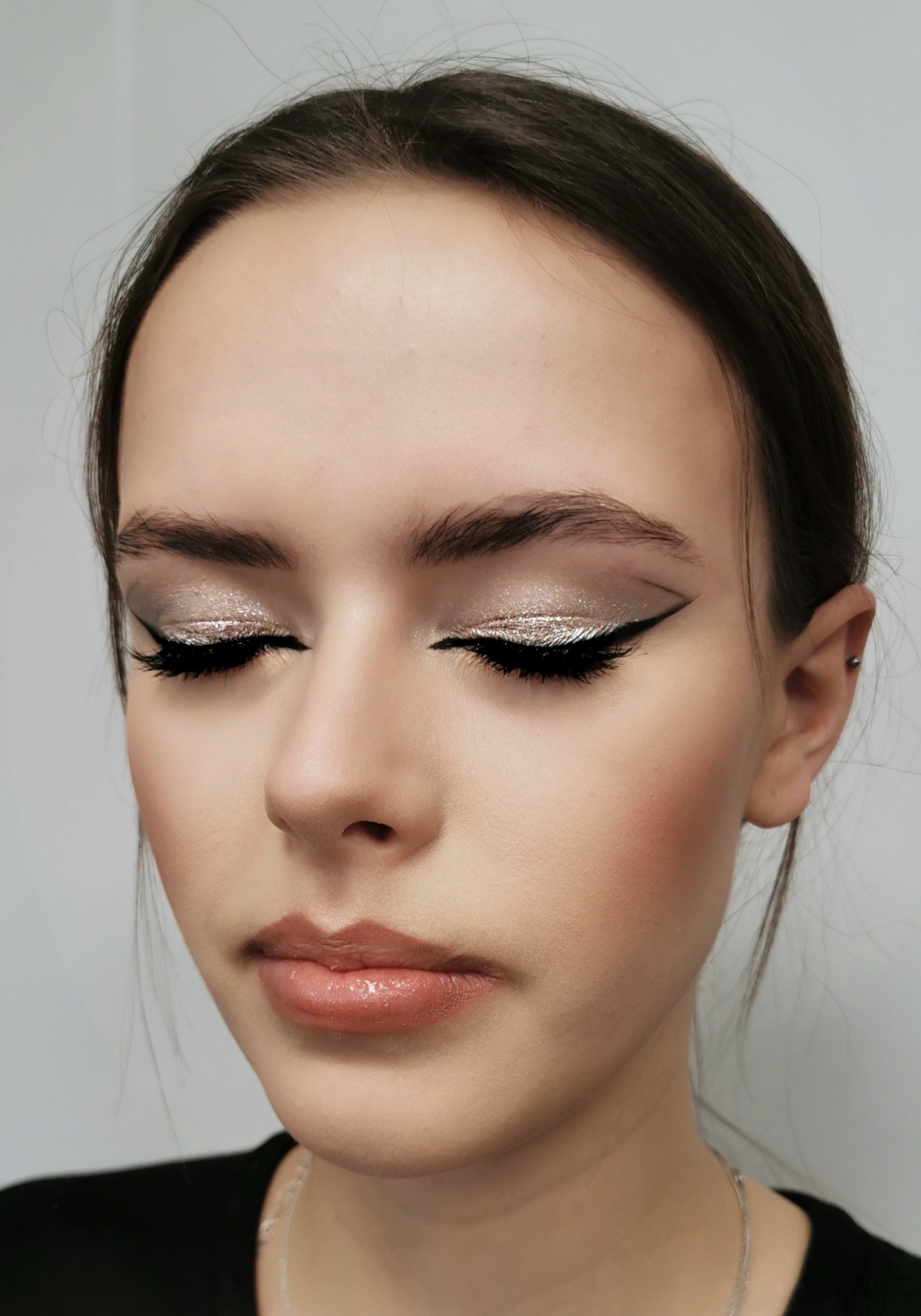 Portret kobiety z zamkniętymi oczami, prezentujący srebrzysty cień do powiek z czarną kreską i błyszczące usta.