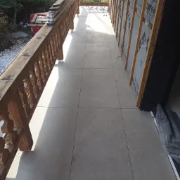 Wyłożony szarymi płytkami taras z drewnianą balustradą w trakcie zabudowy balkonu, widoczne ocieplenie ściany z listwami i folią.