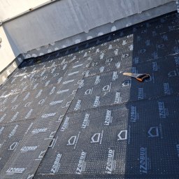 Flat Roof Pawel Canert - Układanie papy termozgrzewalnej IZOBUD na dachu. Widoczna piła ręczna i fragment osoby. Praca dekarska w trakcie, z bliska, z detalami materiału.