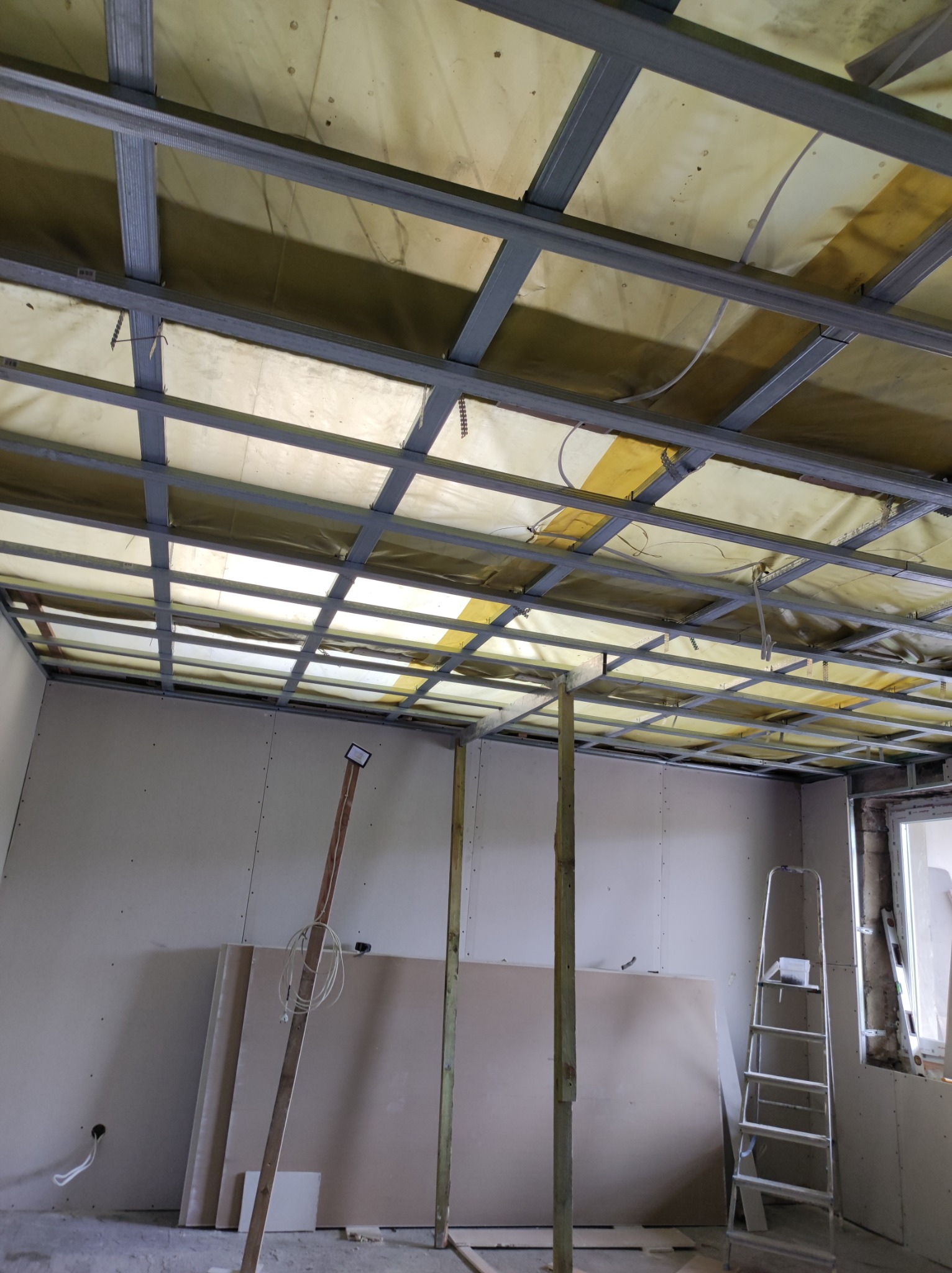 Montaż stelaża sufitu podwieszanego z płyt karton gips w Szczecinie, widoczne profile metalowe, izolacja oraz częściowo zamontowane płyty na ścianach.