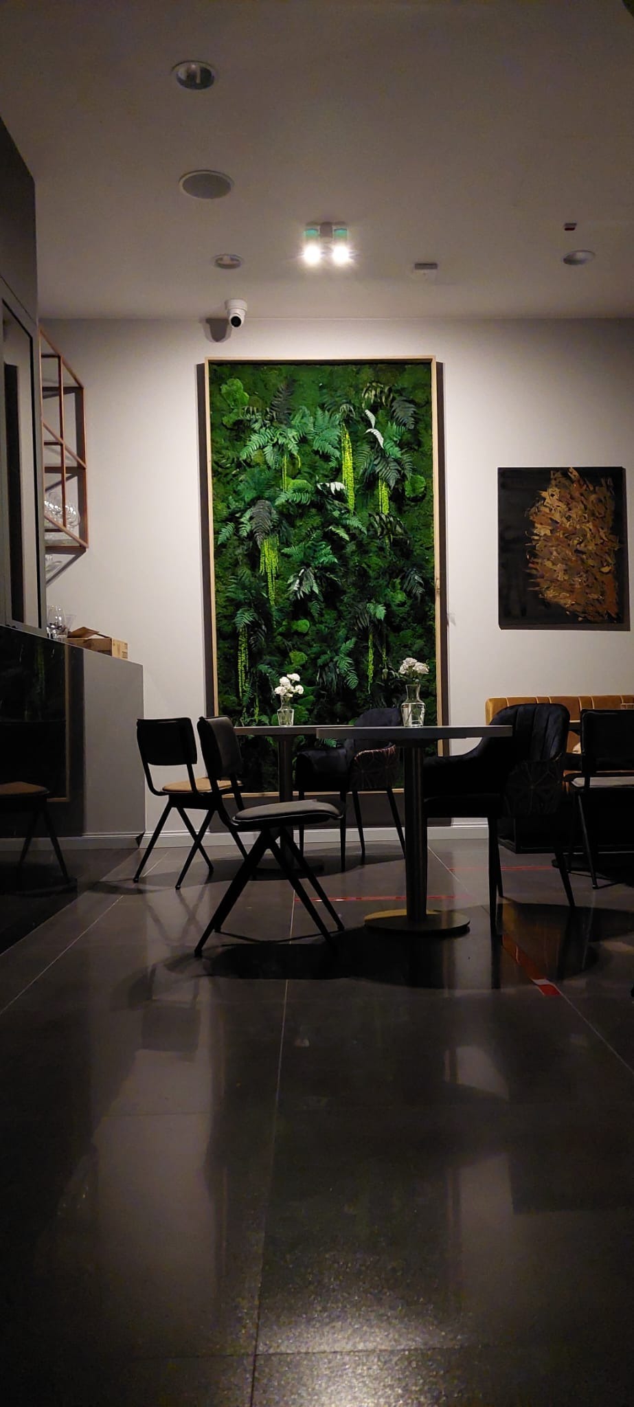 Wnętrze lokalu w Krakowie z dekoracyjną ścianą z roślin, stolikiem i krzesłami, oświetleniem punktowym i polerowaną podłogą.