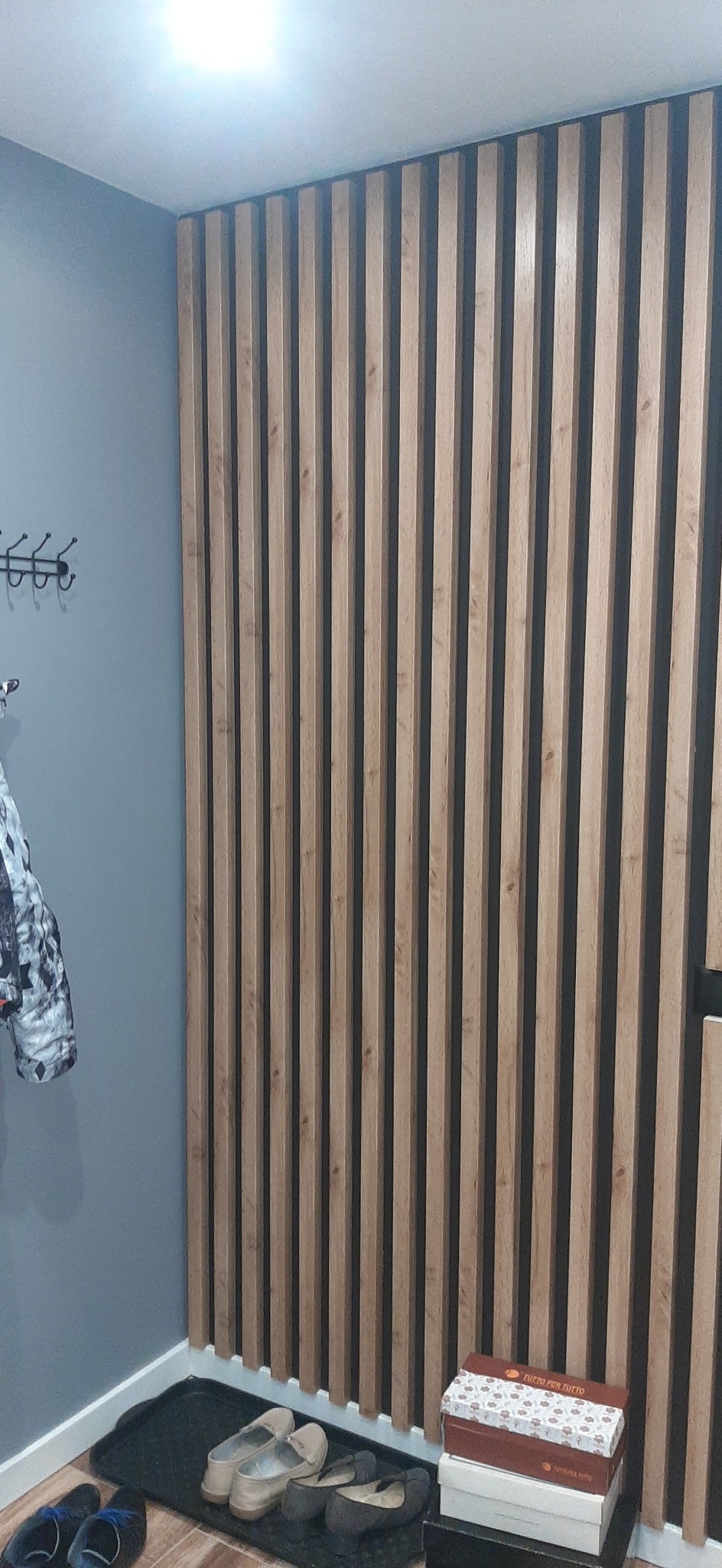Dekoracyjna ściana z drewnianych lameli w przedpokoju, widoczne buty i wieszak na ubrania.