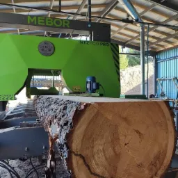 Obróbka kłody na traku taśmowym MEBOR HTZ1100 PRO, widoczny przekrój poprzeczny z wyraźnymi słojami, otoczenie hali.