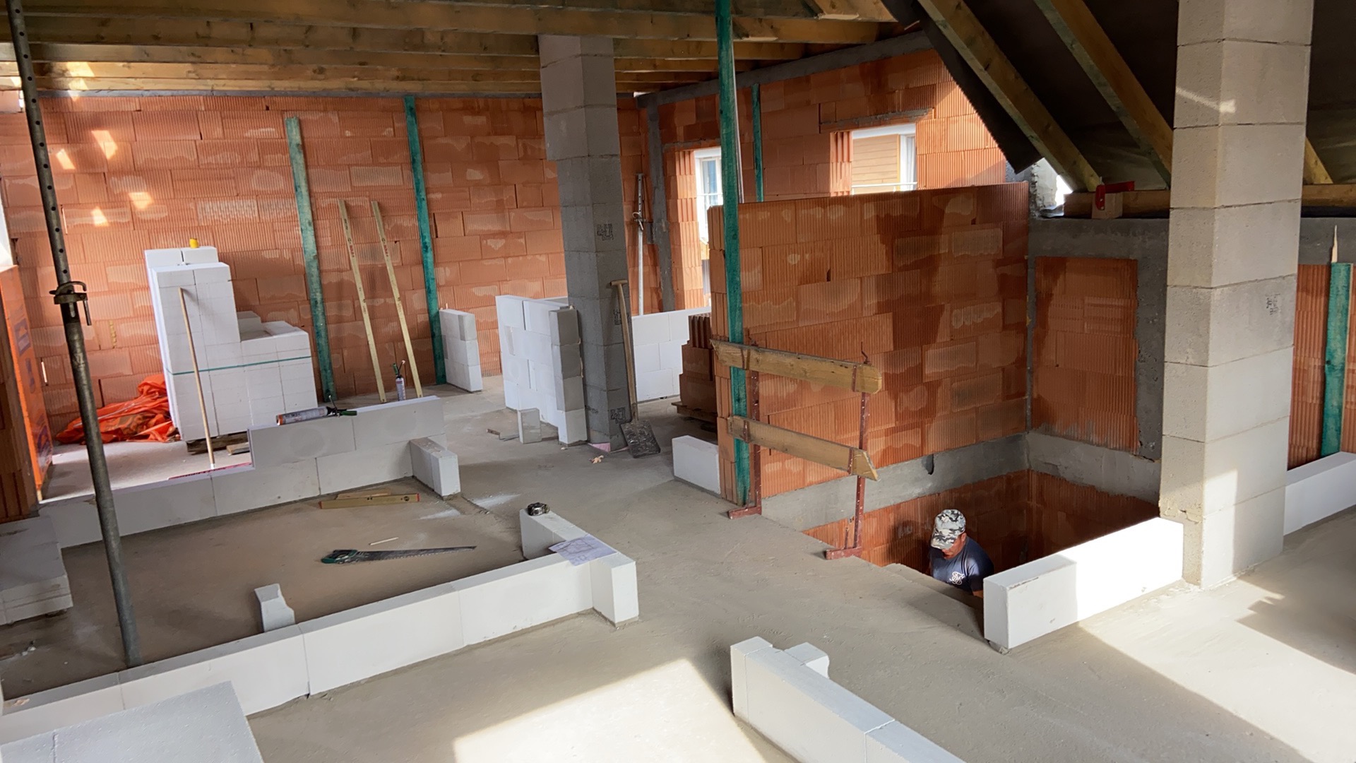 Wnętrze w trakcie budowy w Połańcu, widoczne ściany z czerwonej cegły i białe bloczki, drewniane stemple podtrzymujące konstrukcję, oraz pracownik w wykopie.