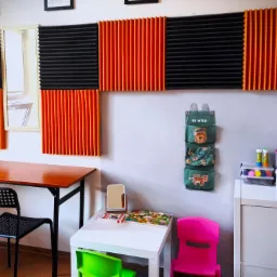 Pokój terapeutyczny z panelami akustycznymi w kolorze czarnym i pomarańczowym, stolikiem z puzzlami, biurkiem z czarnym krzesłem, szafką z zabawkami i organizerem ściennym z motywem zwierzęcym.