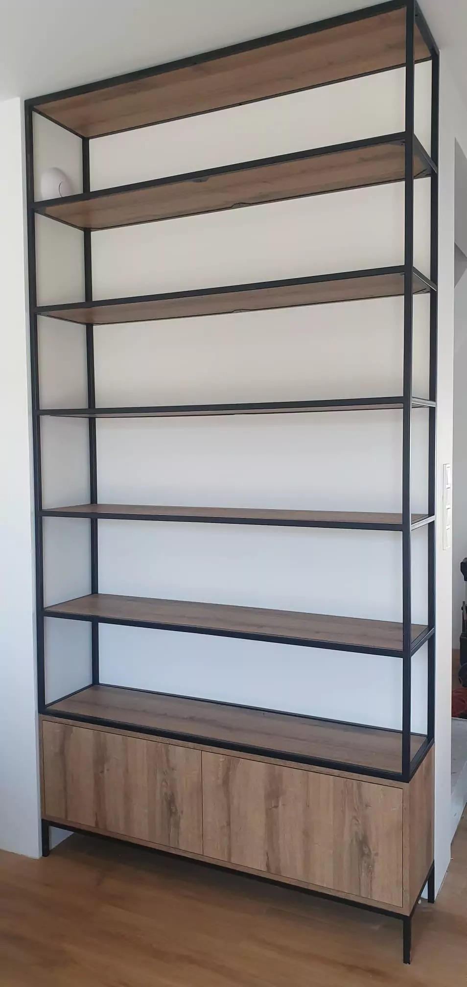 Regał na wymiar z drewnianymi półkami i szafką, czarna metalowa konstrukcja, minimalistyczny design, wnęka w ścianie.