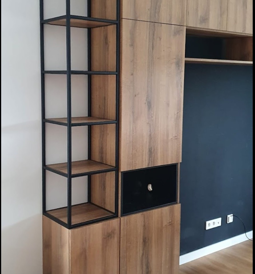 Zabudowa ściany z drewnopodobnymi frontami, czarnym panelem i metalowym regałem z półkami, na tle ciemnej ściany i jasnej podłogi.