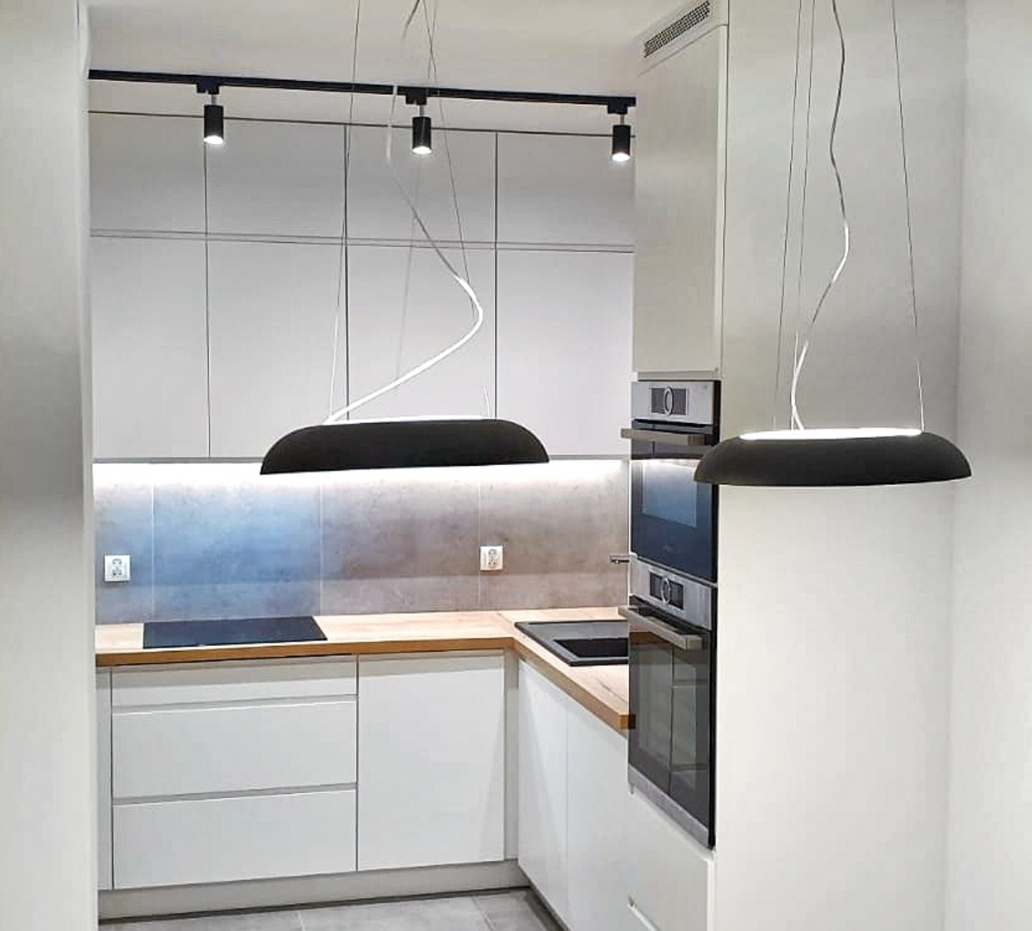 Nowoczesna kuchnia z białymi szafkami, drewnianym blatem i designerskimi lampami wiszącymi o nietypowym kształcie