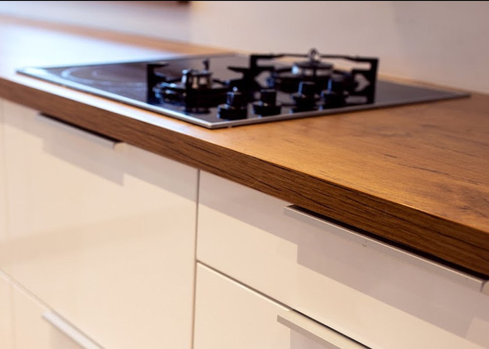 Fragment blatu kuchennego z drewnianym dekorem i wbudowaną płytą grzewczą, białe fronty szafek z minimalistycznymi uchwytami.