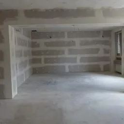 Surowe ściany w nowo wykończonym pokoju z widocznymi płytami gipsowo-kartonowymi, przygotowane do dalszych prac wykończeniowych, z widocznym oknem w tle.