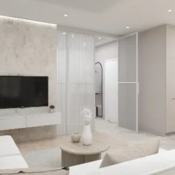 Jasne wnętrze salonu z aneksem kuchennym w minimalistycznym stylu. Na pierwszym planie sofa z beżowymi poduszkami, okrągły stolik kawowy i telewizor na ścianie o fakturze betonu. W tle widoczne...