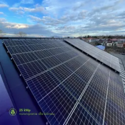 Panele fotowoltaiczne na dachu budynku, widok z góry, błękitne niebo z chmurami w tle, logo 25 kWp rozwiązanie dla biznesu w lewym dolnym rogu.