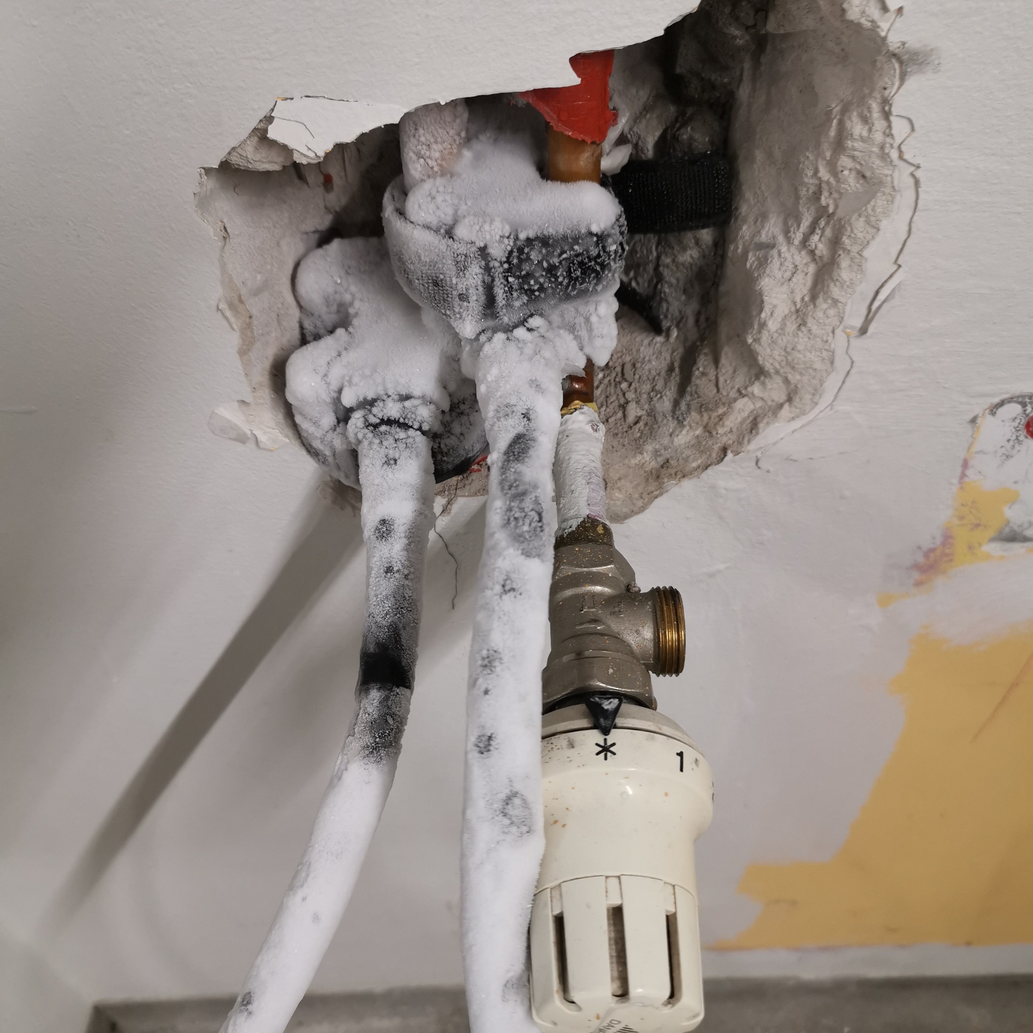 Zamrożone rury instalacji grzewczej wystające z dziury w suficie, widoczny zawór termostatyczny z ustawieniem na '1'.