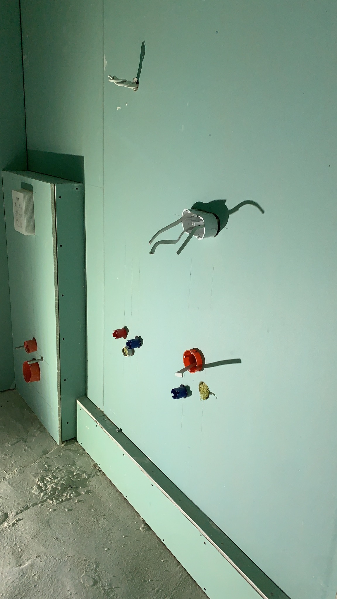 Ściana z zielonej płyty gipsowo-kartonowej z wystającymi przewodami elektrycznymi i instalacjami hydraulicznymi w trakcie montażu w łazience.