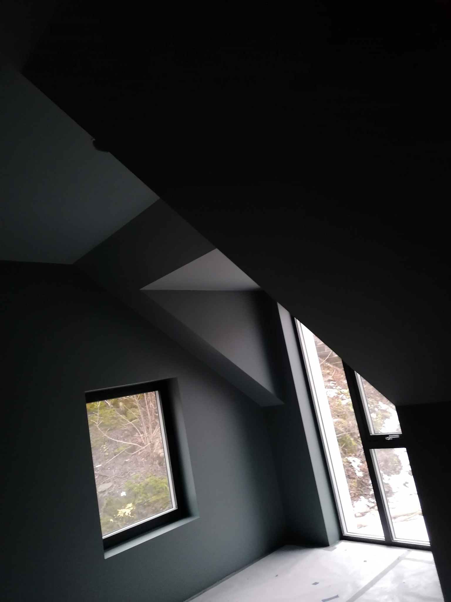 Poddasze po remoncie z dwoma oknami o różnej wielkości, pomalowane na szaro, widok na zimowy krajobraz za oknem.