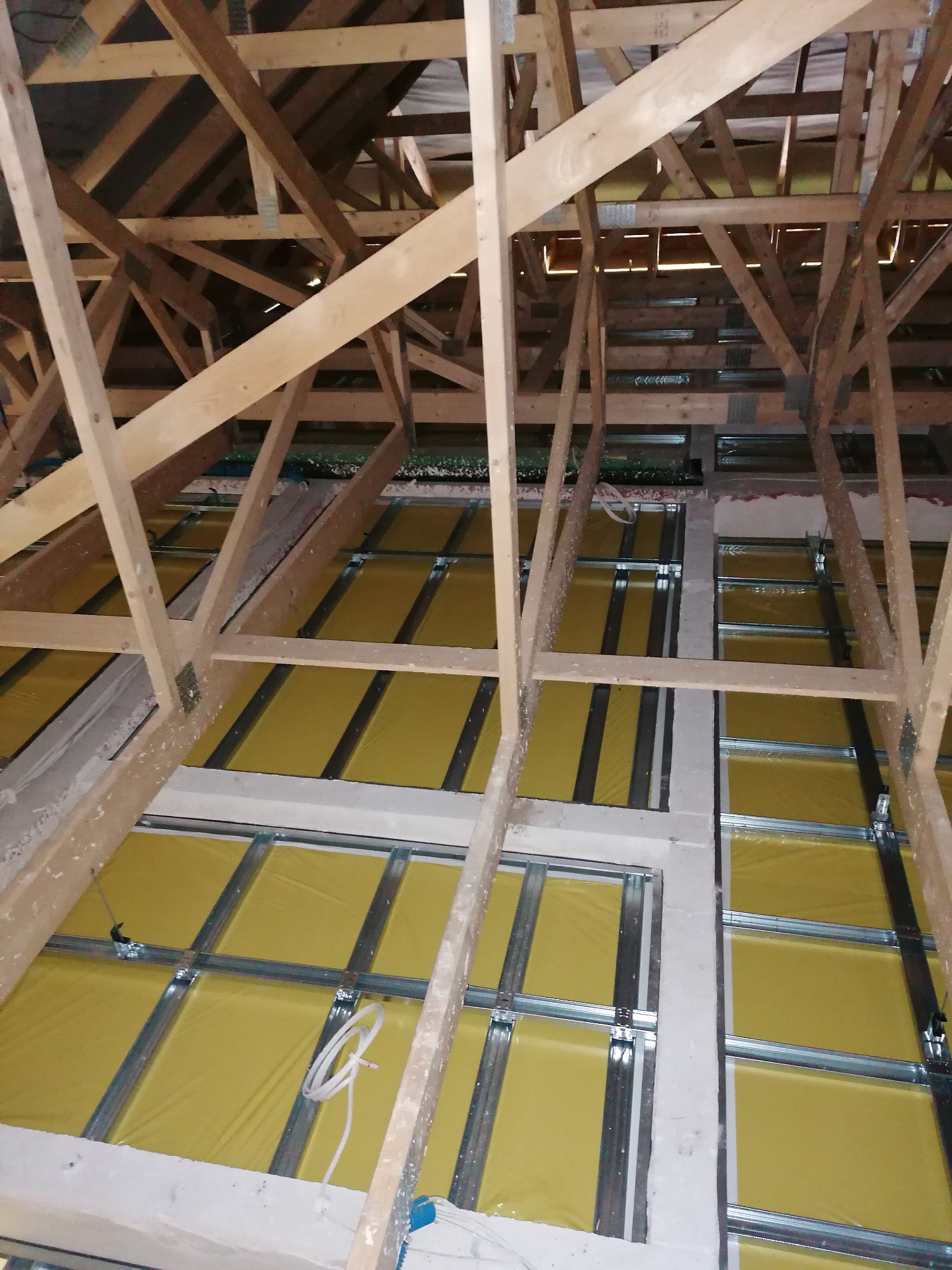 Szkielet drewniany poddasza z widoczną izolacją w kolorze żółtym i metalowymi profilami przygotowanymi do montażu płyt gipsowo-kartonowych, widok z dołu.