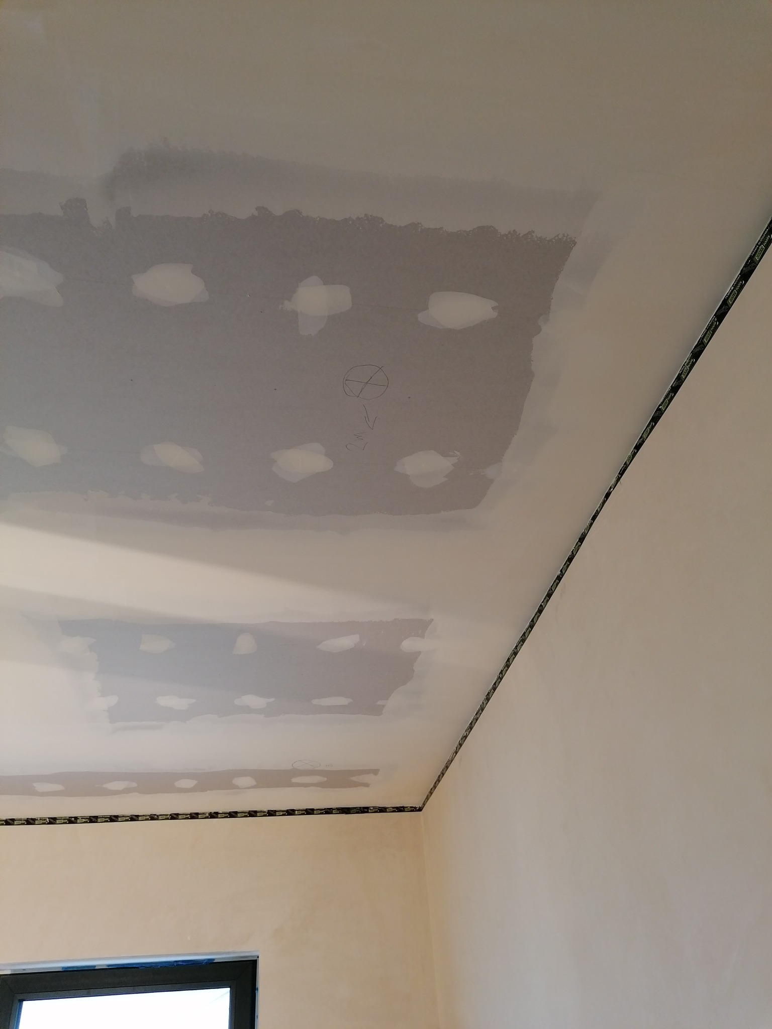 Niedokończony sufit z płyt kartonowo-gipsowych, widoczne miejsca szpachlowania i zaznaczenia ołówkiem, listwa wykończeniowa przy ścianie.