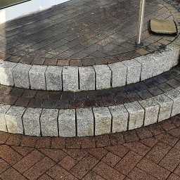 Firma ogólnobudowlana - Dwu-stopniowe schody wejściowe wykończone kostką granitową i ceglaną, prowadzące do drzwi, z widoczną kostką ułożoną w jodełkę na podeście.