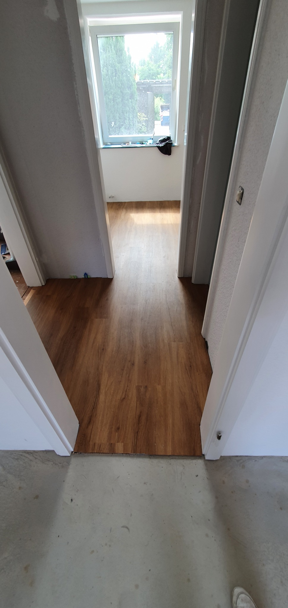 Układanie paneli podłogowych w Gnieźnie, widok z progu na świeżo położoną, drewnopodobną podłogę w korytarzu, ściany w trakcie przygotowania do malowania, okno dachowe w tle.