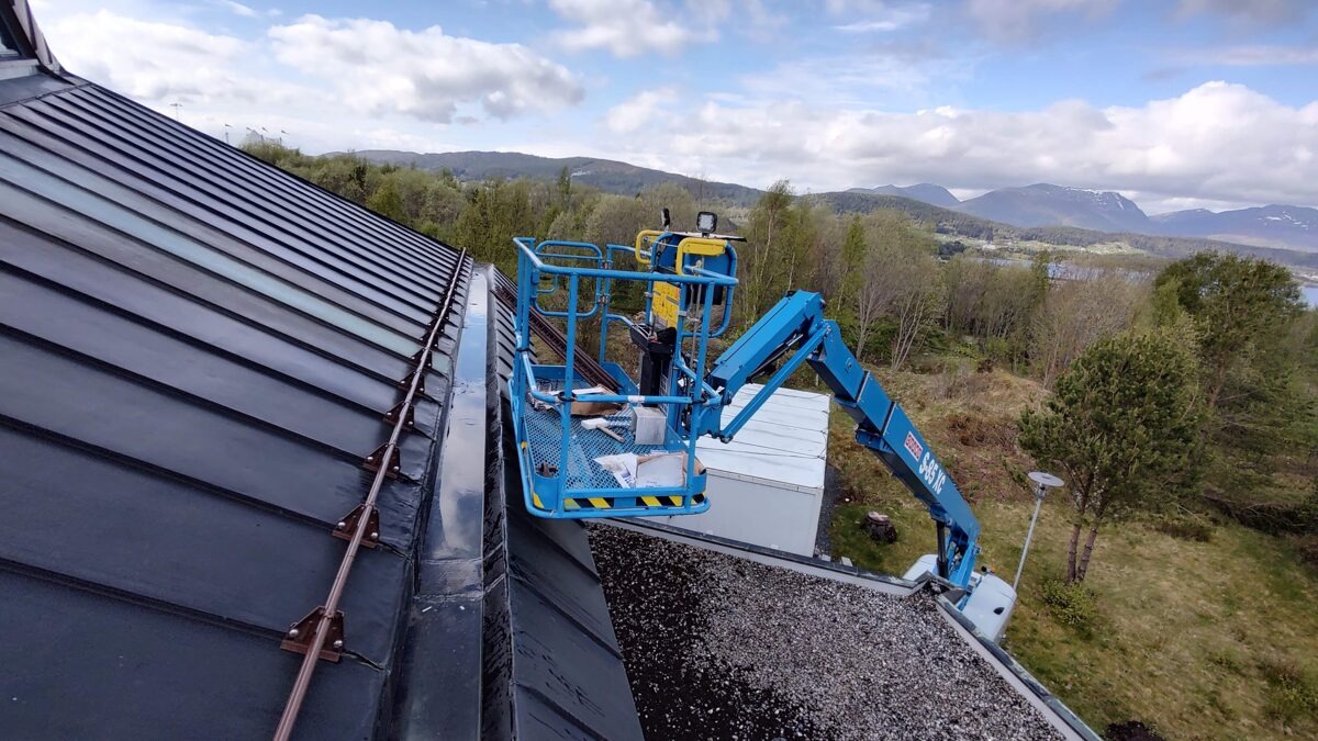 Prace dekarskie przy dachu z blachy na kościele, widok z podnośnika koszowego na rynny i otaczający krajobraz.
