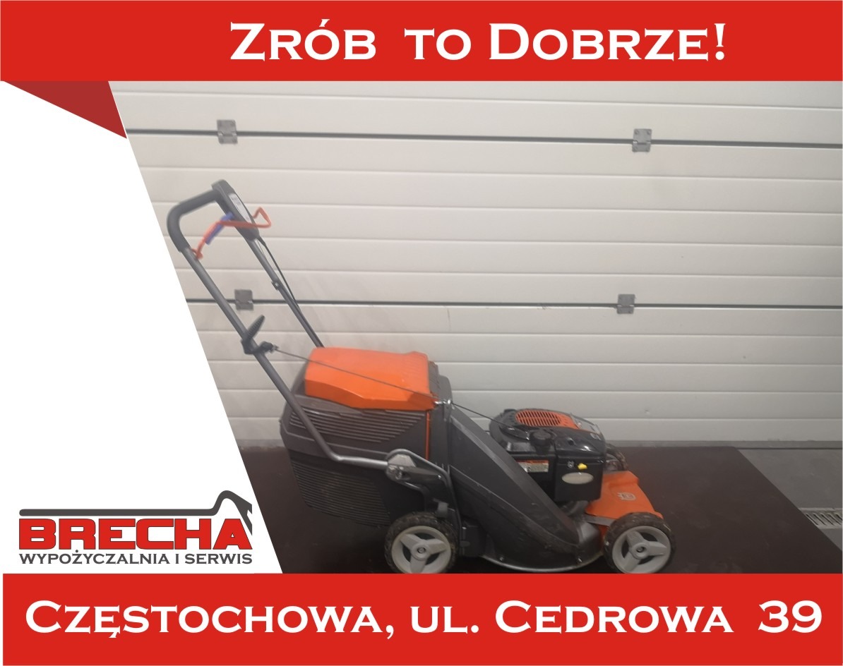 Pomarańczowo-szara kosiarka spalinowa z koszem na tle białej bramy garażowej, prezentowana przez firmę Brecha z Częstochowy.