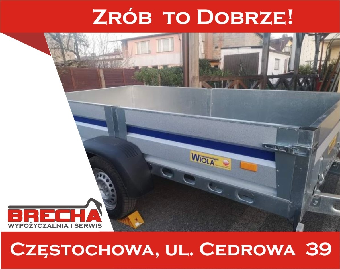 Przyczepa budowlana marki Wiola, z logo Brecha Wyposażalnia i Serwis Częstochowa, zaparkowana na zewnątrz, z żółtym klinem pod kołem.